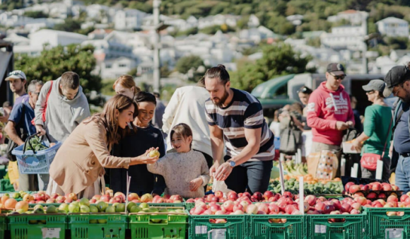 A family picks out apples at a busy farmer's market on a sunny day