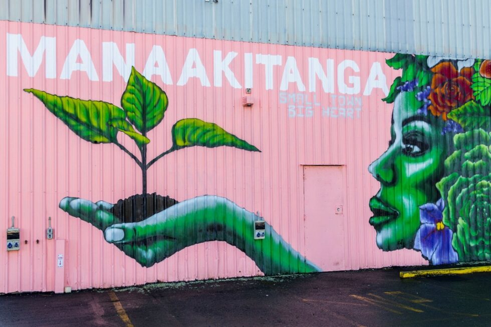 Mural of a nature-themed woman with a handful of soil and a seedling, and the words "Manaakitanga - Small town, big heart"